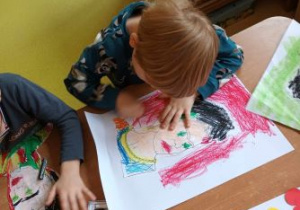 Chłopiec siedzi przy stoliku i rysuje pastelą tło obrazu