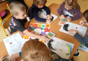 Dzieci siedzą przy stoliku i kolorują pastelami swoje prace
