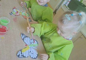 Dziewczynka i chłopiec malują motyle farbami