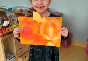 dziewczynka prezentuje swoją pracę w odcienaich koloru pomarańczowego