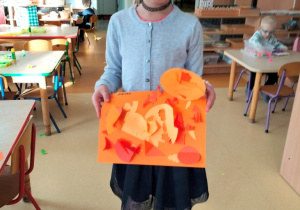 dziewczynka prezentuje swoją pracę w odcienaich koloru pomarańczoweg