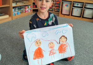 chłopiec prezentuje swoją pracę z namalowaną rodziną