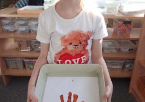 Dziewczynka z misiem na koszulce prezentuje misia wykonanego z odciśniętej dłoni