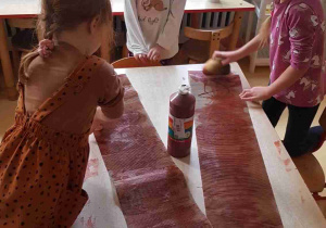 Dziewczynki przygotowują papierowy pień drzewa, malując tekturę brązową farbą