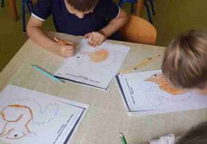 Dzieci siedzą przy stole i kolorują obrazek wiewiórki