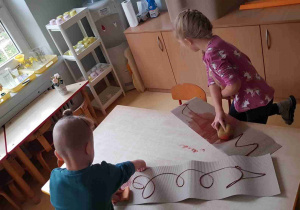 Dziewczynka i chłopiec rozprowadzają brązową farbę na tekturze falistej