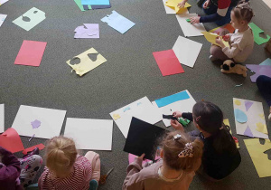 Dzieci siedzą na dywanie, wycinają elementy pracy