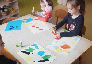 Dziewczynki przyklejają kolorowe papierowe elementy na karton