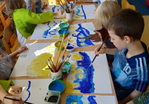 Dzieci siedzą przy stoliku i malują farbami