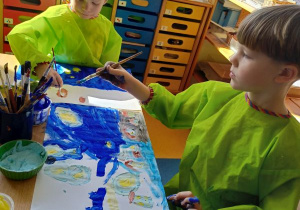 Chłopcy siedzą przy stole i malują farbami