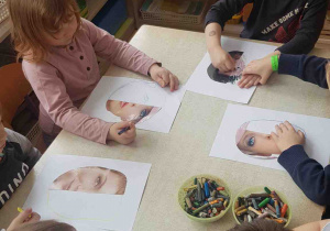 Dzieci siedzą przy stoliku i rysują twarz