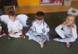 Dzieci siedzą na dywanie w oczekiwaniu na Uroczystość Wigilijną