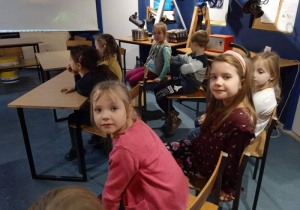 Dzieci siedzą na krzesełkach, cztery dziewczynki patrzą w stronę osoby, która zrobiła zdjęcie.