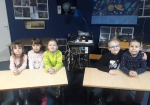 Trzy dziewczynki siedzą przy jednym stoliku, dwóch chłopców przy drugim stoliku. dzieci uśmiechają się.