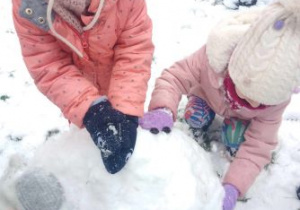 Dziewczynki dolepiają śnieg do bałwana