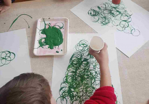 Chłopcy malują choinki odbijając papierowe kubeczki umoczone w zielonej farbie
