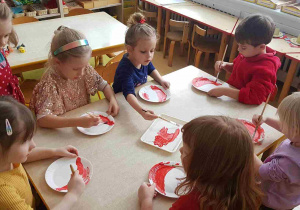 Dzieci malują papierowe talerzyki, z których powstaną Mikołaje