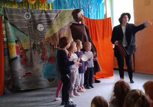 Grupa dzieci stoi na scenie z instrumentami obok przebranych aktorów