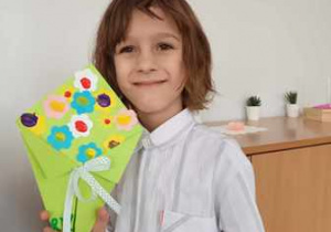 Chłopiec pozuje do zdjęcia i trzyma w dłoniach bukiet dla Babci i Dziadka wykonany z elementów kolorowego papieru