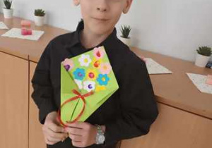 Chłopiec prezentuje wykonany przez siebie z kolorowego papieru bukiet dla Babci i Dziadka