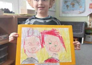 Chłopiec prezentuje narysowany przez siebie portret Babci i Dziadka
