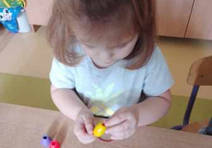 Dziewczynka podczas wykonywania pracy na pomocy edukacyjnej nawleka żółty koralik na sznurek