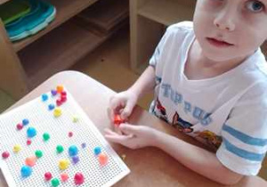 Chłopiec siedzi przy stoliku i układa mozaikę
