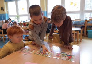 Trzech chłopców siedzi przy stoliku i dopasowuje obrazki do ilustracji.