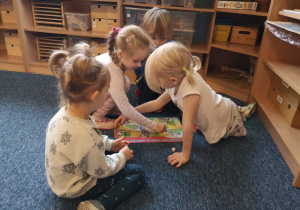 Trzy dziewczynki i jeden chłopiec siedzą na dywanie i grają w grę planszową
