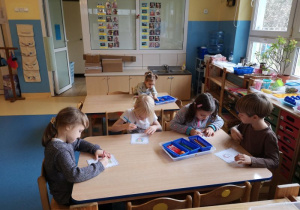 Dzieci siedzą przy stolikach i kolorują obrazki