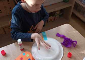 Chłopiec precyzyjnie dokleja paski bibuły do talerzyka papierowego w czasie zabawy plastycznej