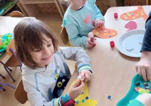 Dziewczynka i chłopiec doklejają kropki z kolorowego papieru do swojej pracy plastycznej