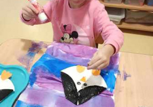 Dziewczynka dokleja elementy kolorowego papieru do swojej pracy plastycznej