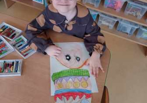 Dziewczynka rysuje pastelami olejnymi siebie podczas zabawy plastycznej