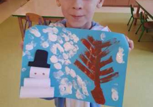 Chłopiec prezentuje wykonaną przez siebie pracę plastyczną przedstawiającą zimowy krajobraz