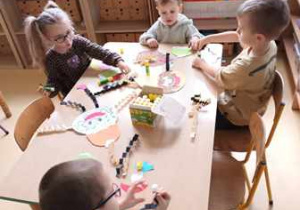 Dzieci siedzą przy stoliku i doklejają elementy kolorowego papieru do pracy plastycznej pt. "Donuts"