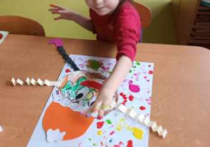 Dziewczynka stempluje palcem kolorowe kropki na swojej pracy plastycznej