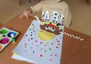 Chłopiec uzupełnia swoją pracę plastyczną i stempluje kolorowe kropki dookoła swojego pączka
