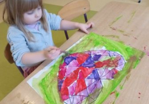 Dziewczynka podczas malowania farbami przy użyciu pędzelka