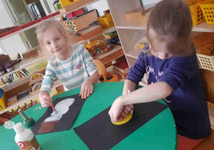 Dziewczynki tworzą bałwanki na czarnych kartkach papieru