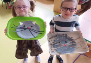 Dziewczynka i chłopiec prezentują swoje koty wykonane z papierowych talerzyków
