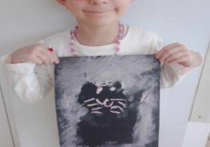 Jagódka pozuje do zdjęcia trzymając w ręku swoją pracę przedstawiającą czarnego kota