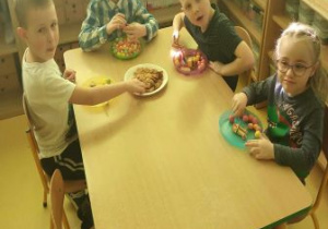 Dzieci siedzą przy stoliku i jedzą tort urodzinowy oraz inne smakołyki