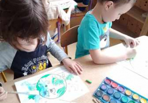 Chłopcy w czasie wykonywania pracy plastycznej malują farbami akwarelowymi ilustrację przedstawiającą planetę Ziemię