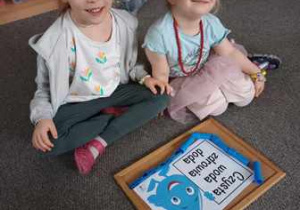 Dziewczynki siedzą na dywanie i układają ramkę z niebieskich klocków do hasła "Czysta woda zdrowia doda"