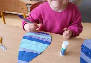 Dziewczynka podpisuje swoim imieniem wykonaną przez siebie pracę plastyczną przedstawiająca kroplę wody