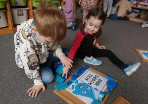 Dziewczynka i chłopiec układają ramkę z niebieskich klocków do hasła dotyczącego wody