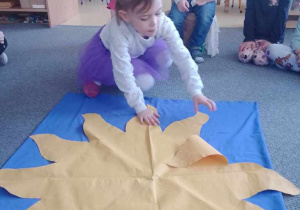 Dziewczynka rozkłada na dywanie "Urodzinowe Słoneczko", w tle widać jubilata