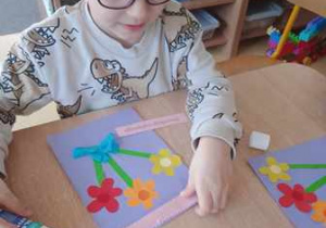 Chłopiec dokleja elementy kolorowego papieru do swojej pracy plastycznej