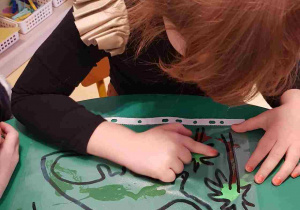 Dziewczynka rozprowadza palcem farbę na planszy z dinozaurem